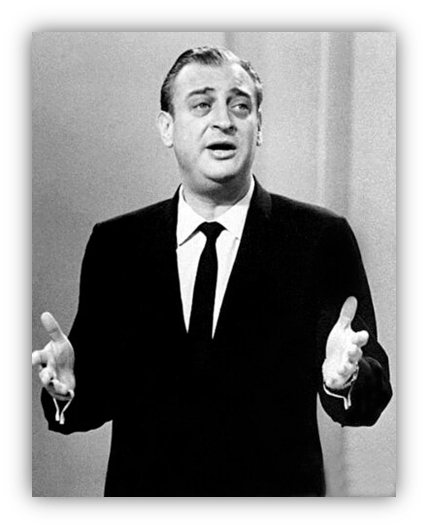 "Black and white image of a comedian performing on stage in a suit."