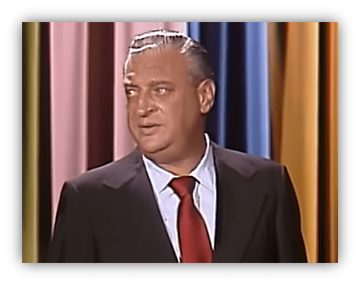 Rodney Dangerfield performing stand-up comedy on stage.