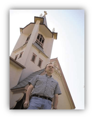 Man standing in front of a church tower on a clear day.