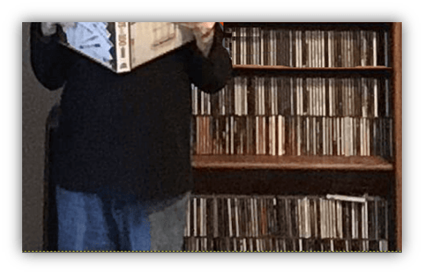 Person holding a music album in front of a shelf filled with CDs.