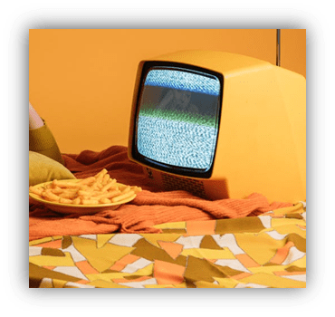 Vintage yellow television with static next to a plate of fries on a colorful tablecloth.