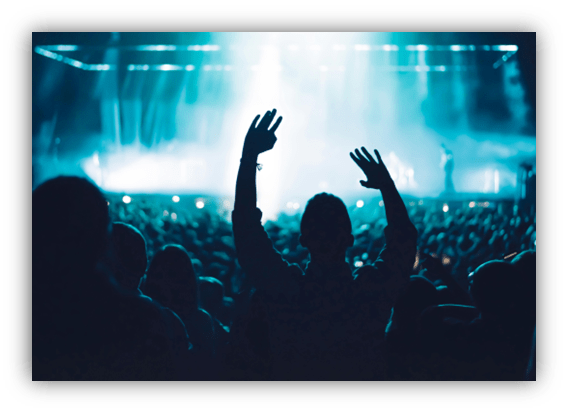 Crowd at a concert with arms raised under dramatic stage lights.