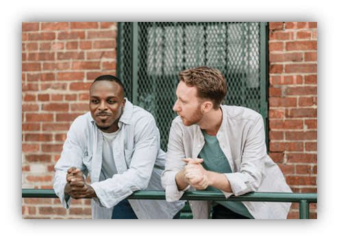 Two men casually leaning on a railing against a brick wall.
