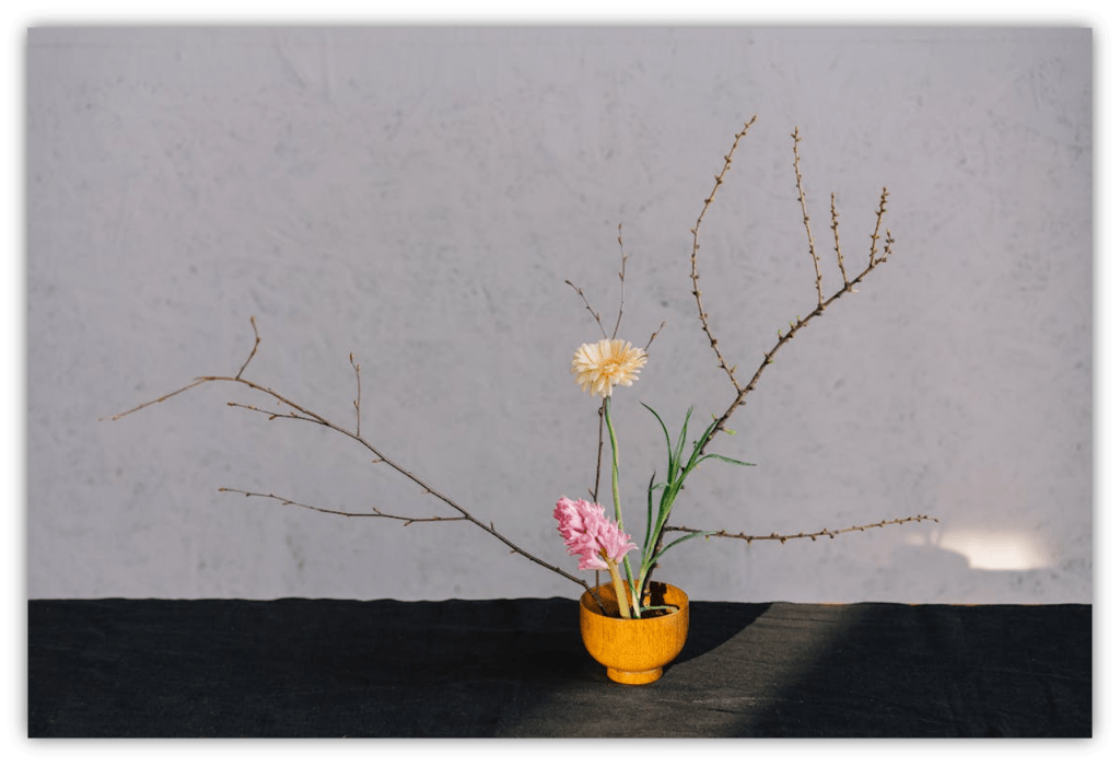 "Minimalist flower arrangement in a yellow bowl with branches and blooms."