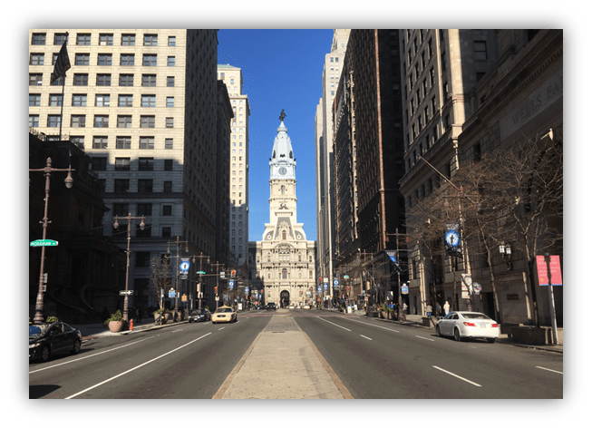 "View of Philadelphia's City Hall on a sunny day, flanked by tall buildings along a busy street."
