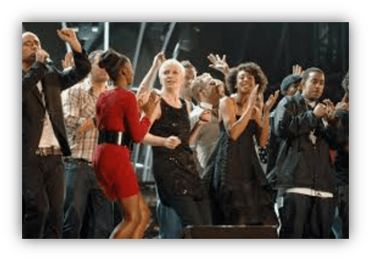 "Group of performers enjoying a live music event, dancing and applauding on stage."