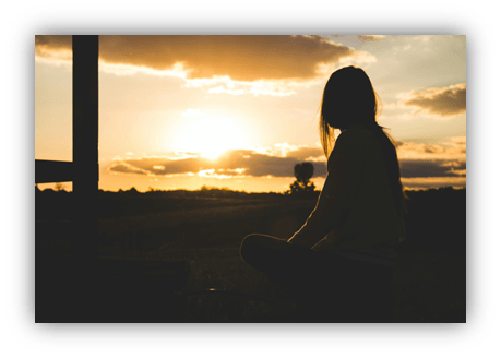 Silhouette of a woman meditating at sunset in a serene landscape.