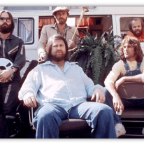 "Group of five men posing outdoors, with a vintage van and plants in the background."
