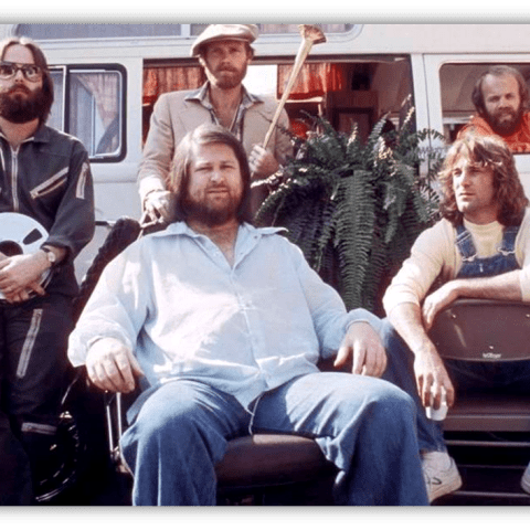 "Group of five men posing outdoors, with a vintage van and plants in the background."