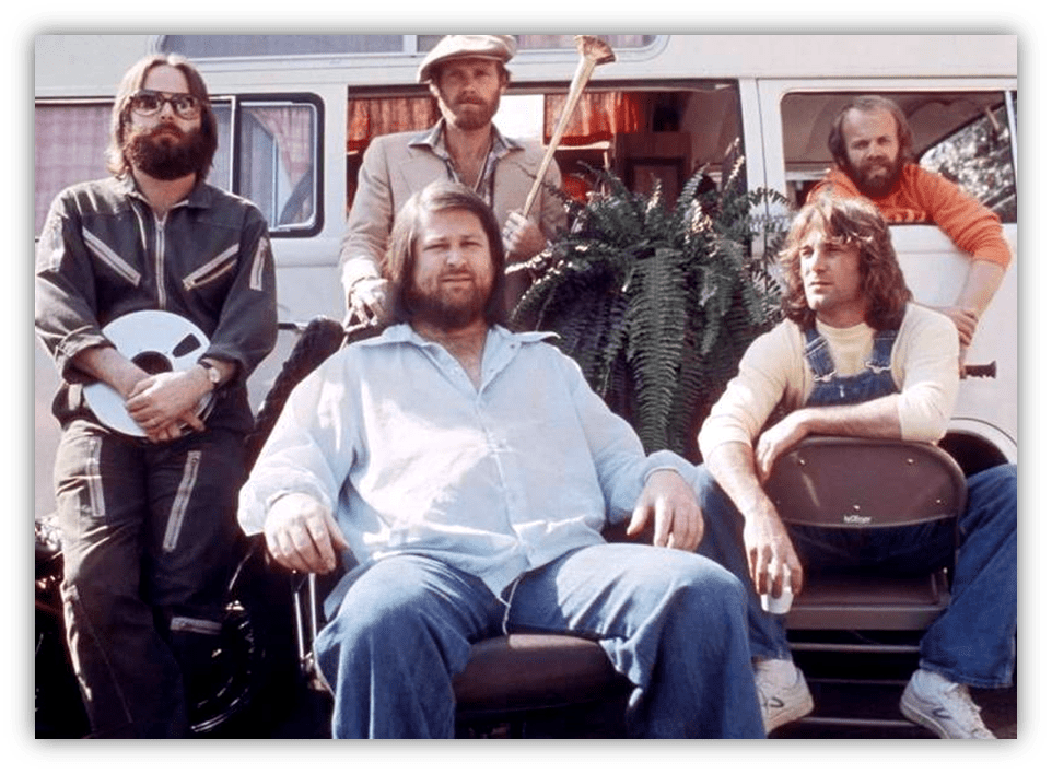 "Group of five men posing outdoors, with a vintage van and plants in the background."