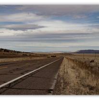 "Empty highway stretching through a dry landscape under a cloudy sky."