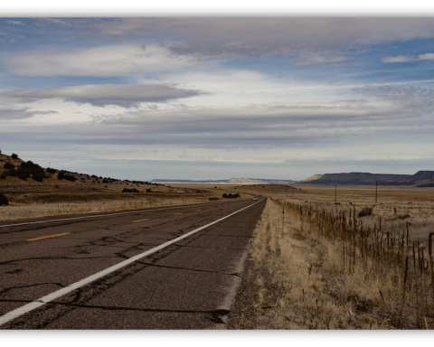 "Empty highway stretching through a dry landscape under a cloudy sky."