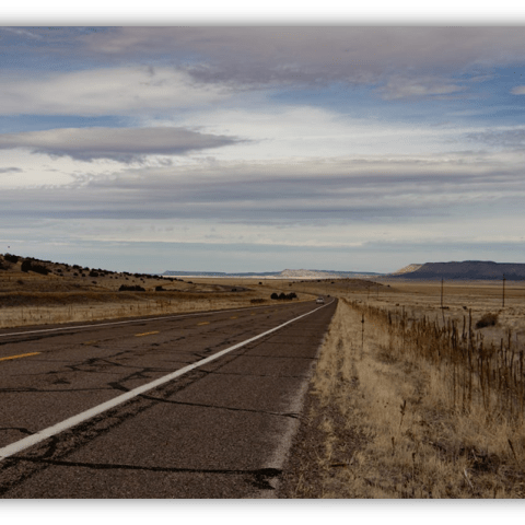 "Empty highway stretching through a dry landscape under a cloudy sky."