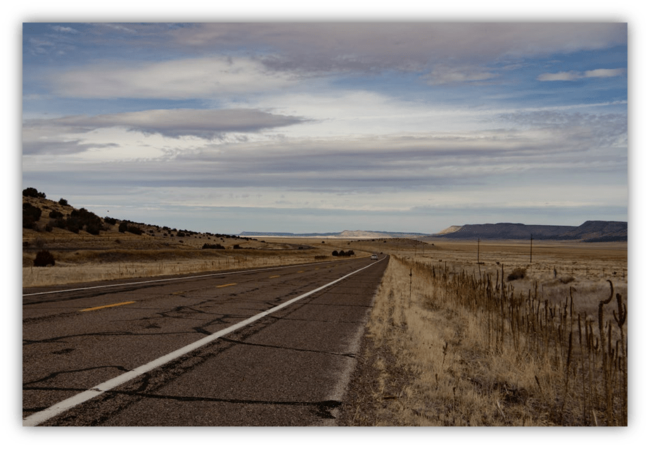 "Empty highway stretching through a dry landscape under a cloudy sky."