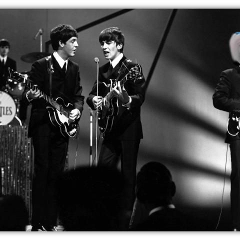 The Beatles performing live on stage in black and white.
