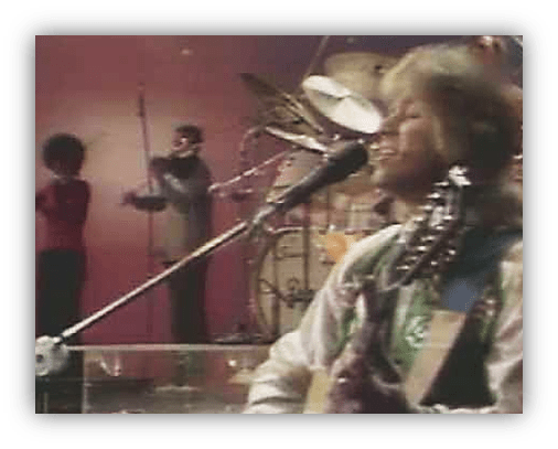 "Musician performing live with band on stage, 1970s music show."