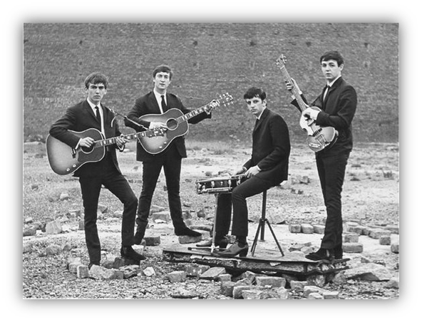"Four musicians in black suits performing outdoors with guitars and drums."