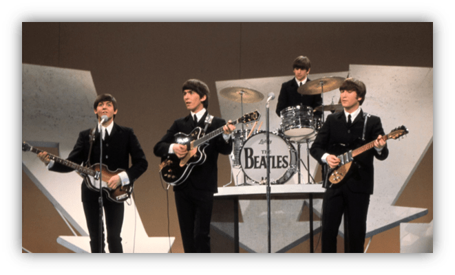 The Beatles performing on stage in 1960s attire.