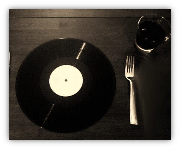 "Vinyl record on a wooden table with a glass of drink and fork."