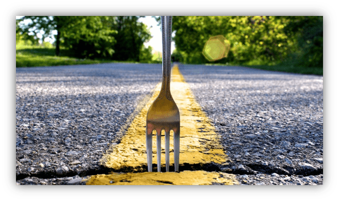 Fork embedded in a yellow line on an empty road surrounded by greenery.