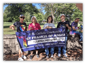 Four people holding a banner for St. Francis of Assisi LGBTQ+ Ministry, promoting inclusivity in a park setting.