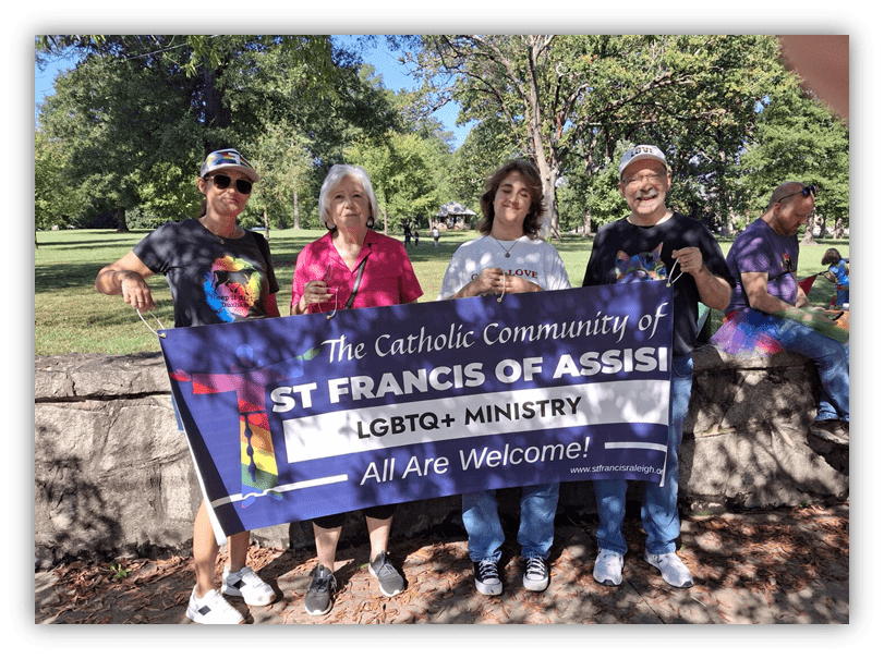 Four people holding a banner for St. Francis of Assisi LGBTQ+ Ministry, promoting inclusivity in a park setting.