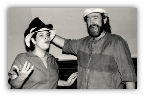 "Two performers joyfully interacting in a black and white photo, both wearing hats."