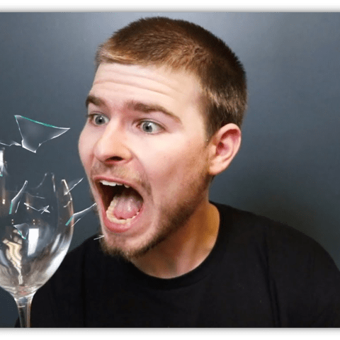"Surprised man reacting to a shattering glass, with fragments flying."