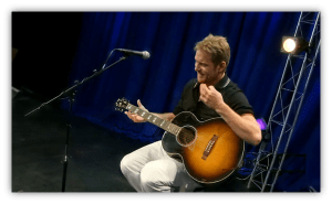 Musician performing with an acoustic guitar on stage.