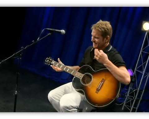 Musician performing with an acoustic guitar on stage.
