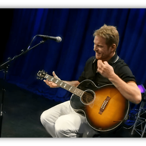 Musician performing with an acoustic guitar on stage.