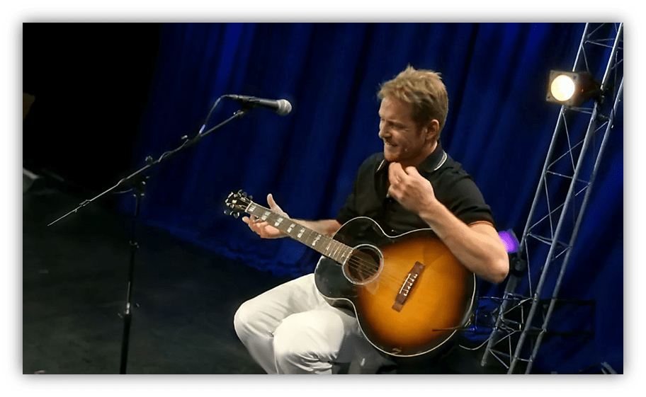 Musician performing with an acoustic guitar on stage.