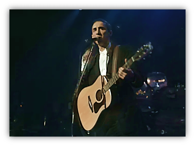 Musician performing live with an acoustic guitar on stage.