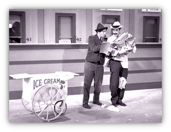 Two men discussing a newspaper in front of an ice cream cart in a vintage black-and-white setting.