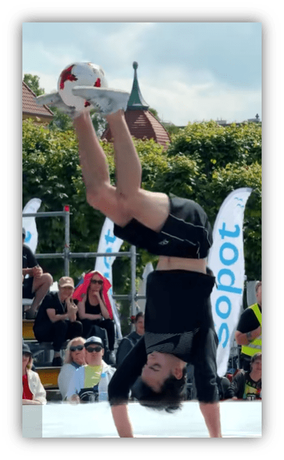 Freestyle footballer performing a handstand while juggling a soccer ball at a competition.