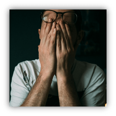 "Person covering face with hands in low light setting."