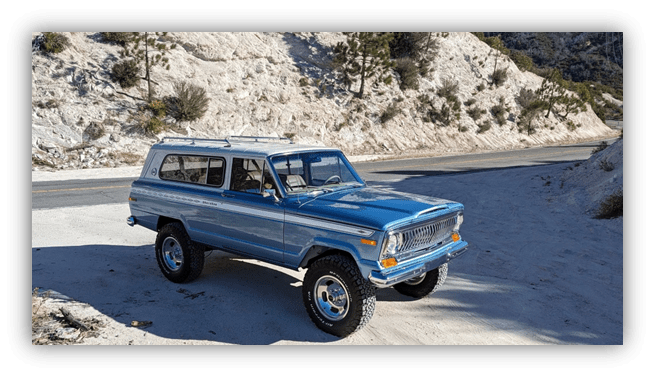 Classic blue SUV parked on sandy road surrounded by rocky terrain.