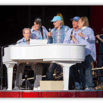 "Musicians performing at a live concert around a white piano."