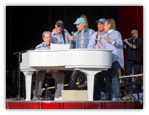 "Musicians performing at a live concert around a white piano."