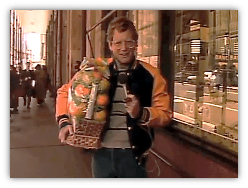 "Letterman holding a large fruit basket while reporting on the street."
