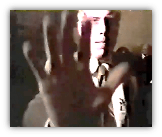 A man blocking the camera with his hand in a dimly lit setting.