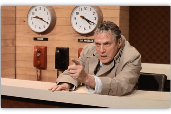 "Angry news anchor gesturing in a studio with clocks for Tokyo and Los Angeles in the background."