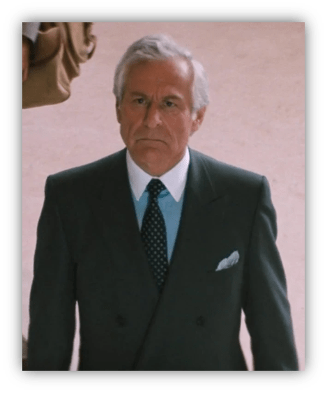 Man in a suit with gray hair, walking with a serious expression.