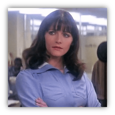 Woman with long dark hair in a blue shirt, looking thoughtfully in an office setting.