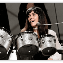 "Smiling female drummer performing with a silver drum set on stage."