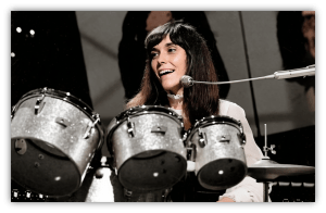 "Smiling female drummer performing with a silver drum set on stage."