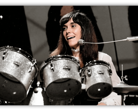 "Smiling female drummer performing with a silver drum set on stage."