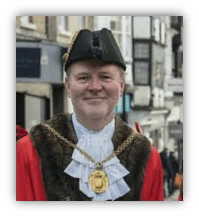 "Mayor in ceremonial attire smiling on a busy street."