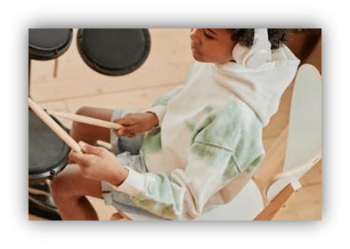 Child playing drums in a cozy hoodie while wearing headphones.