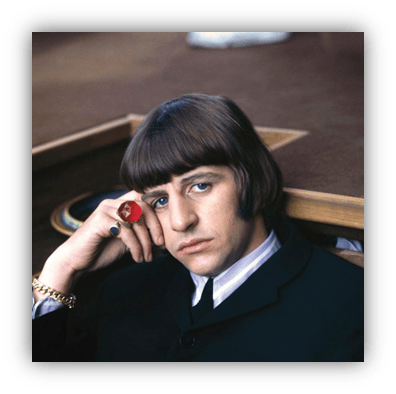 "Young man with a bowl haircut wearing a black suit and a red ring, looking thoughtfully at the camera."